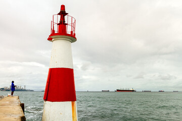 Fisherman standing on a pier next to a lighthouse with freighter boats in Salvador, Brazil