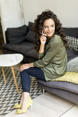Obraz premium Pretty woman with curly hair sitting on the sofa in the room and using a mobile phon