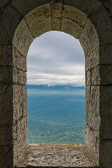 Arch window in the old stone fortress, mountains and sky view
