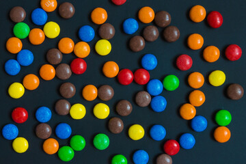 Multicolored sweets in the form of a dragee on a dark background pattern frame background
