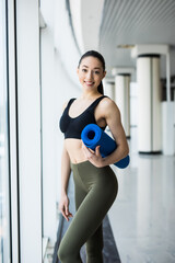 Young happy woman with yoga mat is ready for fitness on panoramic windows background