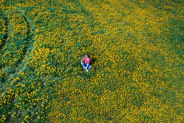 Flight over a girl lying on a green grass in yellow field flowers