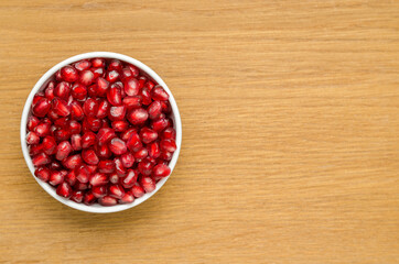 Grains Of Pomegranate In A White Bowl On A Wooden Board. Close-Up. Free Space For Text. Top View. Left Version.