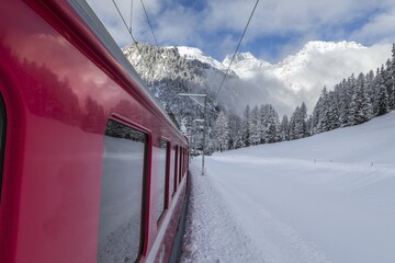 Train going through landscapes covered in snow with mountains and trees, also covered in snow, in the background, non far from Fillisur. Fillisur, Canton of Graubunden, Switzerland.