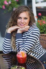 Young beautiful girl outdoors. Pretty woman at the cafe drinking lemonade. Curly hair. Girl smiling at camera and looking forward