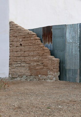 Überreste einer Lehmziegel- oder Adobe-Mauer vor einem Wellblech-Zaun