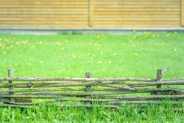 Fototapeta premium A braided wooden fence made of thin branches in the countryside against green lawn at the neat farm