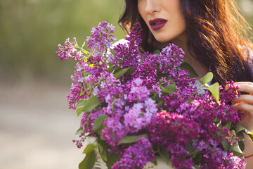 Naklejka premium Beautiful girl outdoors. Pretty young woman with bouquet of lilac.Unrecognizable lady with flowers close up