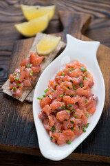 Plate with salmon tartare on a rustic wooden serving board, studio shot, selective focus