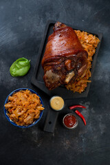 Above view of whole baked pork knuckle with braised cabbage on a wooden serving board, dark metal background, studio shot