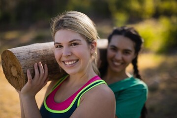 Portrait of trainer and woman carrying heavy wooden log