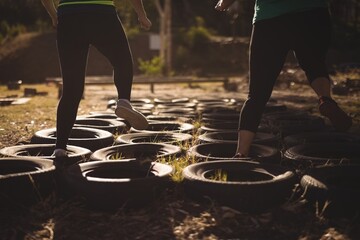 Low section of friends running over tires during obstacle course - obrazy, fototapety, plakaty