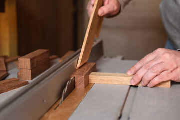 Carpenter sawing wooden plank by circular saw helping with stick for safety