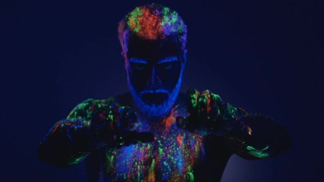 A man with a beard in the ultraviolet light. Magic passes with hands. Close-up of hands. Dance in ultraviolet light. An unreal dance of a man in the ultraviolet light. Strong, muscular man