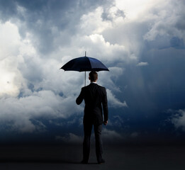 Businessman with umbrella standing over stormy background. Business, protection, crisis concept. © Acronym