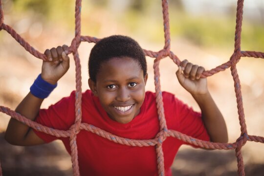 Portrait of happy boy leaning on net during obstacle course