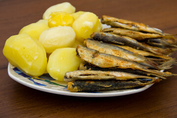 Fried baltic herring with boiled potatoes on a plate on wooden background