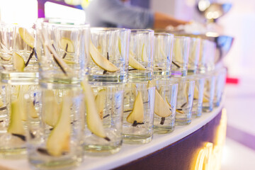 Row of clean glasses for whiskey prepared by the barman for drinks, strong alcohol with slices of fresh delicious pear.