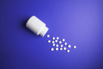 White medical pills on a colored background with a vial