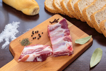Raw pork ribs and spices over a cutting board, beside wholemeal bread slices