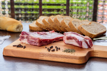 Raw pork ribs and different spices over a wooden cutting board, in front of wholegrain bread and a window