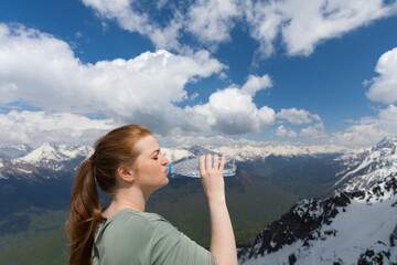 Young woman drink water from plastic bottle in the mountains on the snow peaks bacground