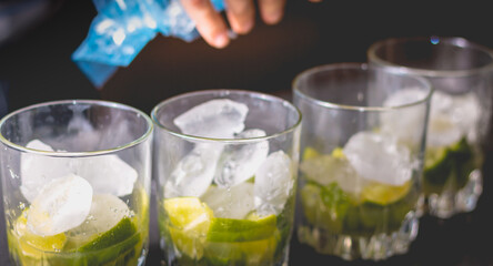 bartender puts ice cubes in glasses of brezillian caipirinha