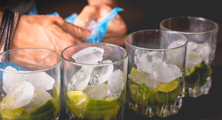 bartender puts ice cubes in glasses of brezillian caipirinha