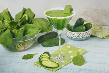 Green spinach and cucumber smoothie on light blue wooden background.