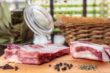 Close-up of raw pork ribs, thyme, black pepper and cloves over a wooden board in front of a window