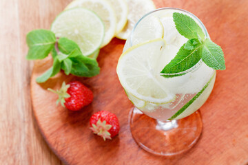 A glass of cold water with lemon and lime, ice cubes and mint leaves