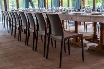 Interior of the restaurant, cafe. Tables with utensils, plates, wiches, knives, glasses and wine glasses, and brown chairs, preparation for celebration. Horizontal frame