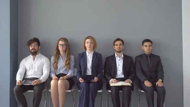 unemployed expect interviews sitting on chairs in the hallway of an office building.