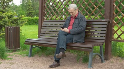 Elderly Man Sitting On Park Bench And Messaging On Mobile Phone