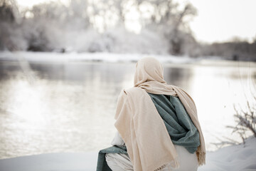 Jesus Christ kneeling next to a river, pondering, in the snow. 