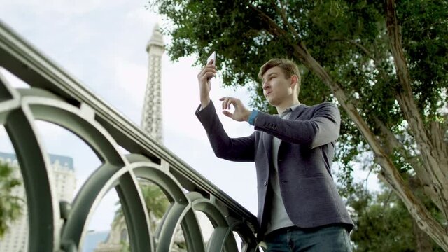 Handsome guy is taking a few photos by using his smartphone with the Eiffel tower on a background
