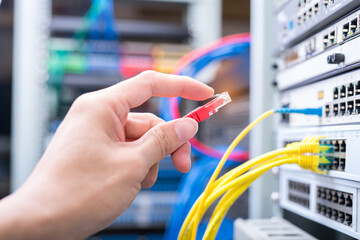 man working in network server room with fiber optic hub for digital communications and internet