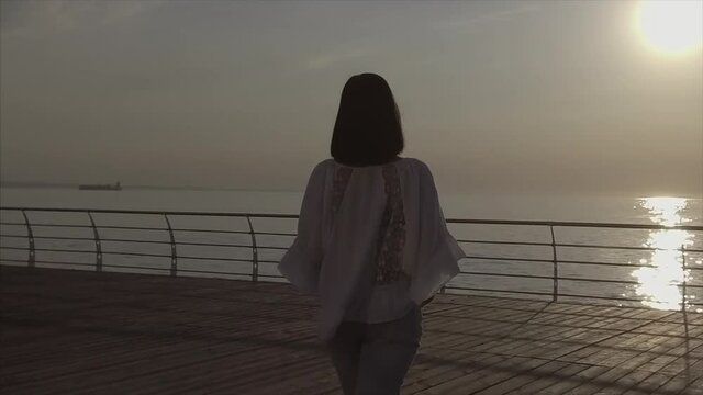The spinning around woman in white beautiful blouse on sunrise background near sea or ocean. Joy and happiness. Slow motion.