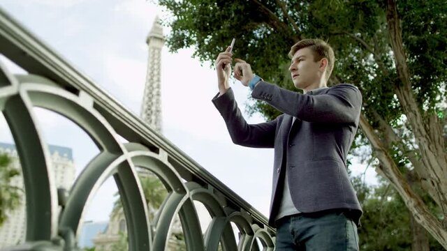 Attractive guy is taking a vacation photos by using his smartphone with the Eiffel tower on a background