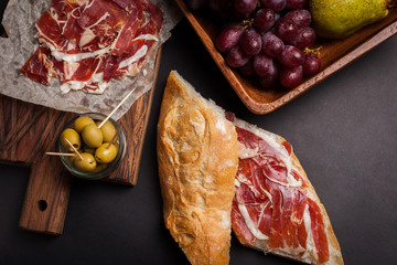 Jamon Iberico with white bread, olives on toothpicks and fruit on a dark background. Top view