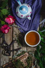 herbal tea on a wooden table with blue and white pot, old keys, roses, wooden desk and herbs, top view