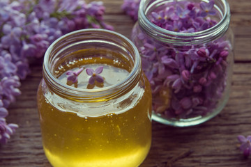 Honey and lilac flowers in glass jars on wooden background