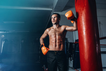 Fototapeta na wymiar Male boxer training in dark gym. Strong Athletic Man Fitness Model Torso showing six pack abs. Portrait of boxer with gloves