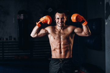 Male boxer training in dark gym. Strong Athletic Man Fitness Model Torso showing six pack abs.