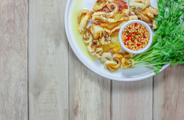 Grilled squid and vegetable with seafood sauce in white plate on wooden table