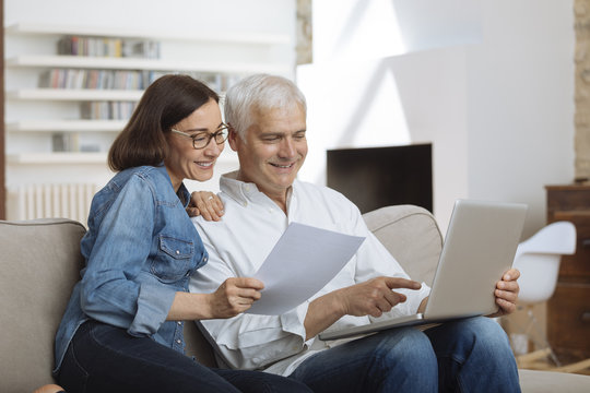 Couple Using Their Laptop To Pay Their Bills At Home In The Living Room