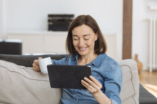 Mature Woman Using Tablet Computer While Relaxing On Sofa At Home