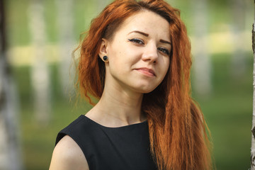 Teenager with problem skin on face. Portret of a young pretty white girl with red curly hair and modern haircut in black dress posing in the birch grove in the village.