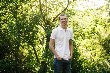 Naklejka na ściany i meble Portrait of a smiling guy in a white shirt against the trees