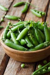 Fresh green peas in a bowl on a wooden background
